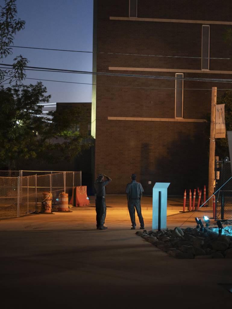 Night view of two men standing at edge of lot near building.