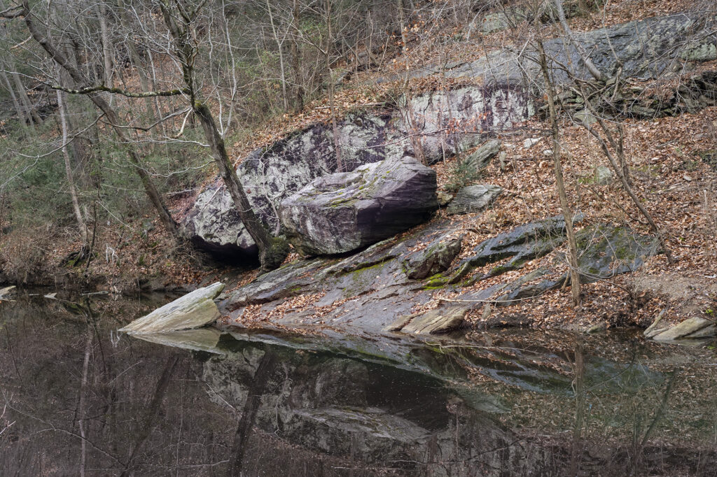 Color view of rocky bank of the Wissahickon Creek mirrored in the water.
