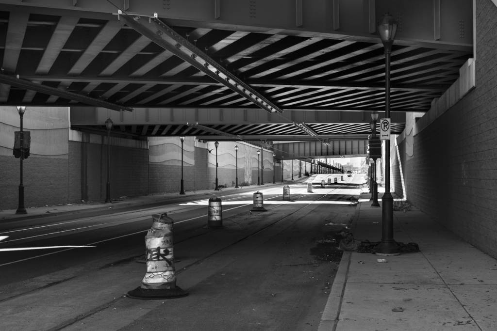 Black and white view of highway passing under overpass, with lanes marked off by traffic barrels.