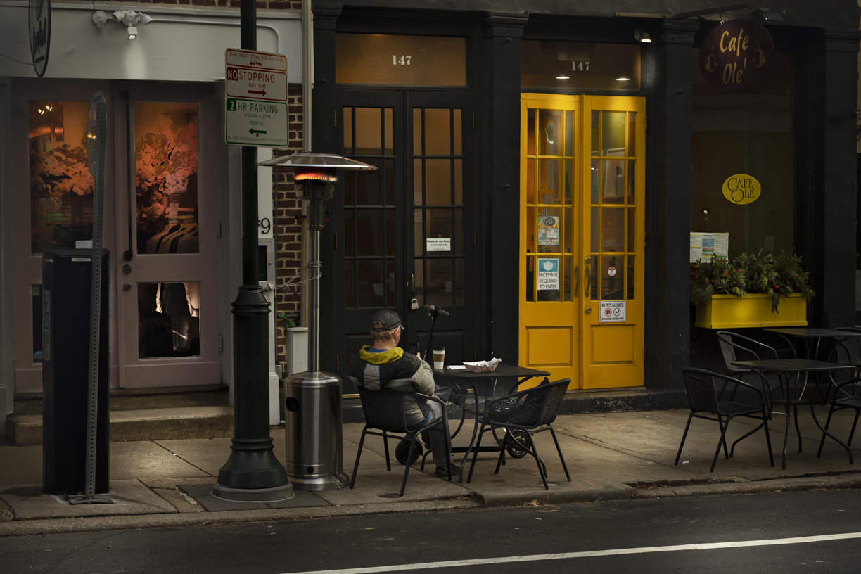 Night view in color of man seated at outdoor café table in colder weather.