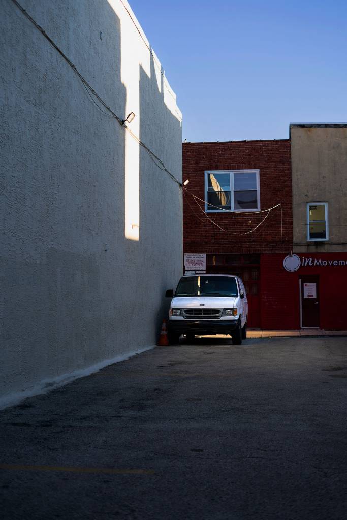 Color view of a white van parked against the wall of a parking lot.