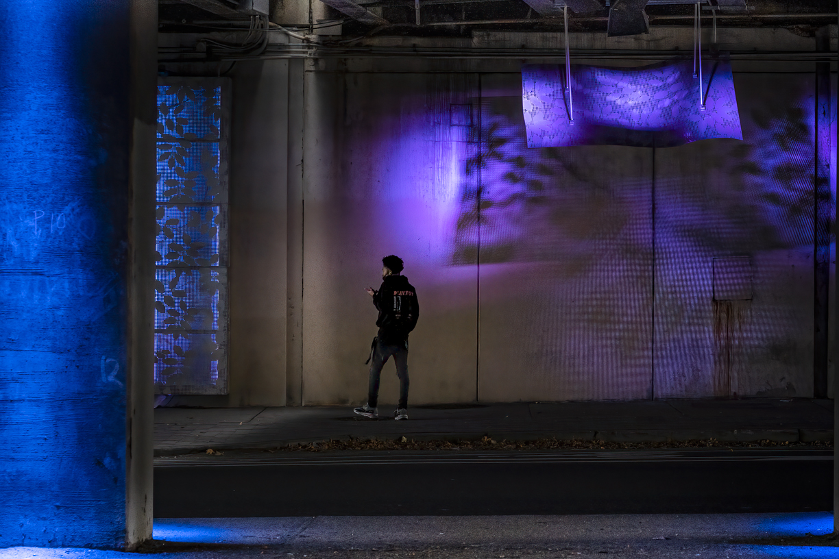 Color view of young Black man standing under an overpass while looking at his mobile phone.
