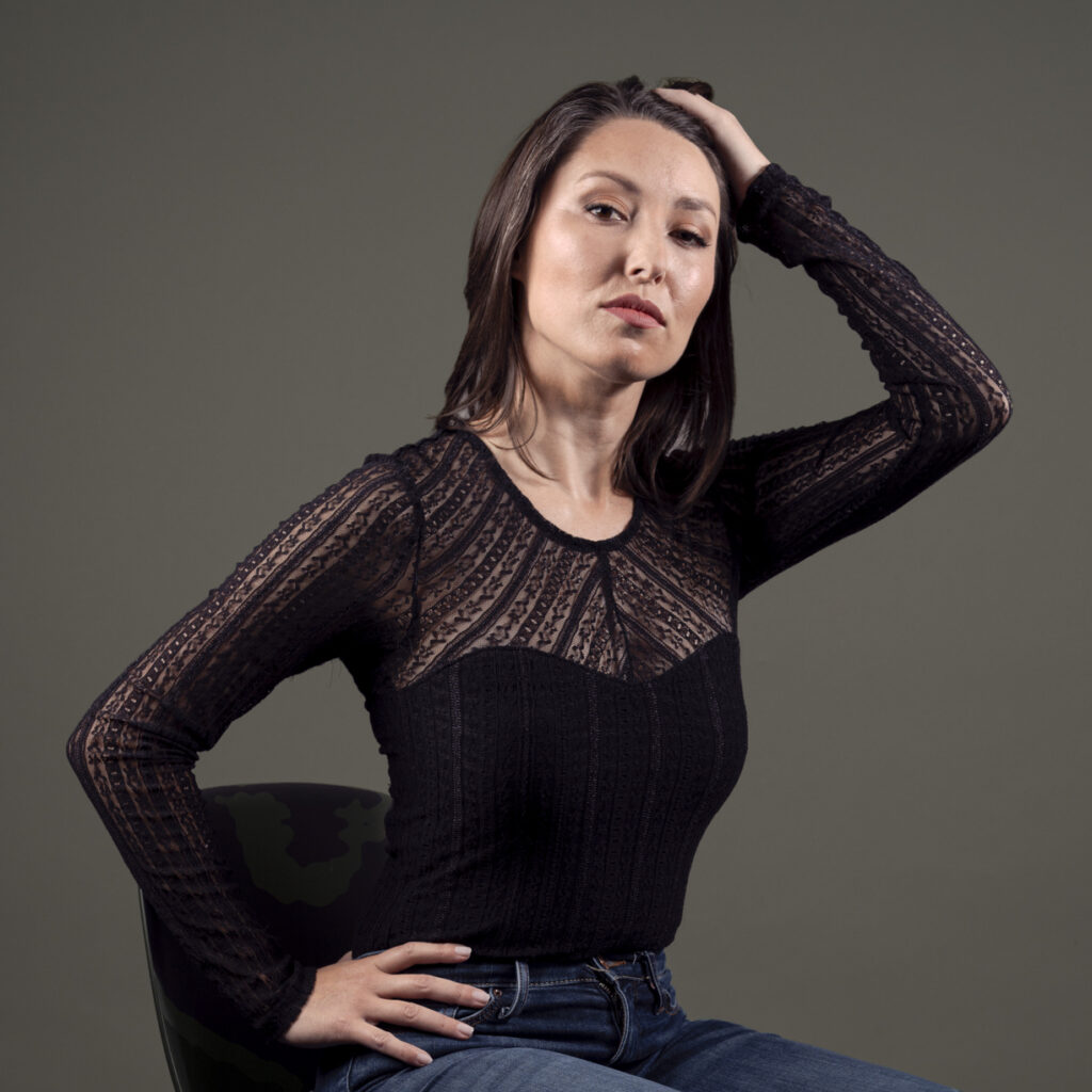 Color portrait of beautiful brunette, seated, with hand on hip.