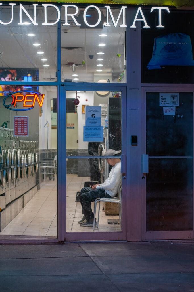 Night view of person sitting inside laundromat with washing machines opposite.