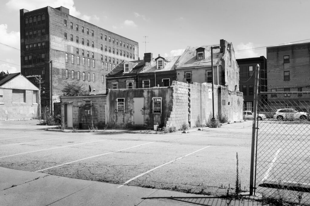 Black and white daylight image of shabby houses surrounded by parking lot